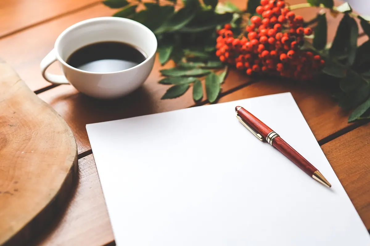 Feuille blanche, stylo et tasse de café posés sur une table en bois