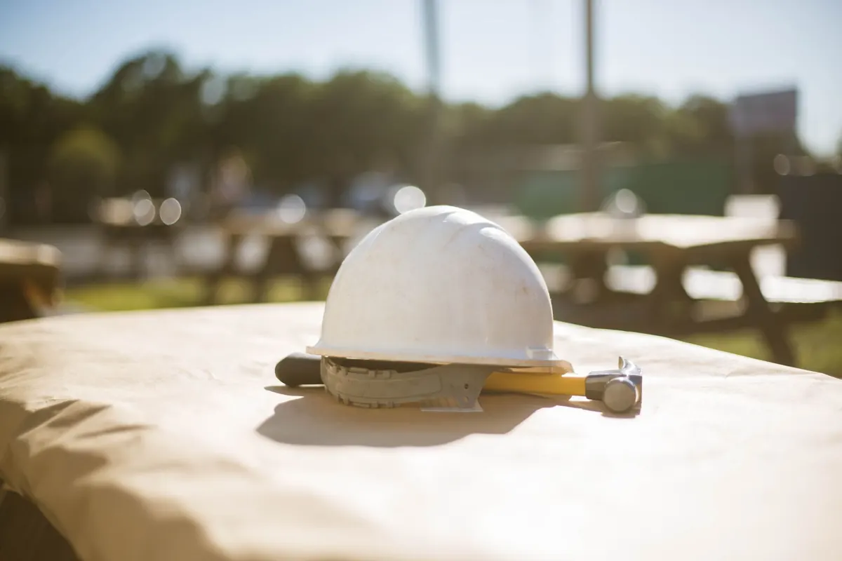 Casque de chantier blanc et marteau posés sur une table baignée de lumière dorée