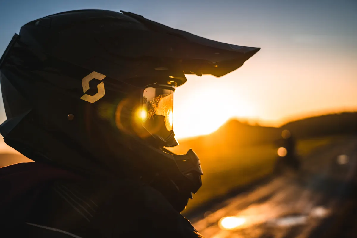 Profil d'un motard casqué à contre-jour devant le soleil couchant, équipement et protection moto