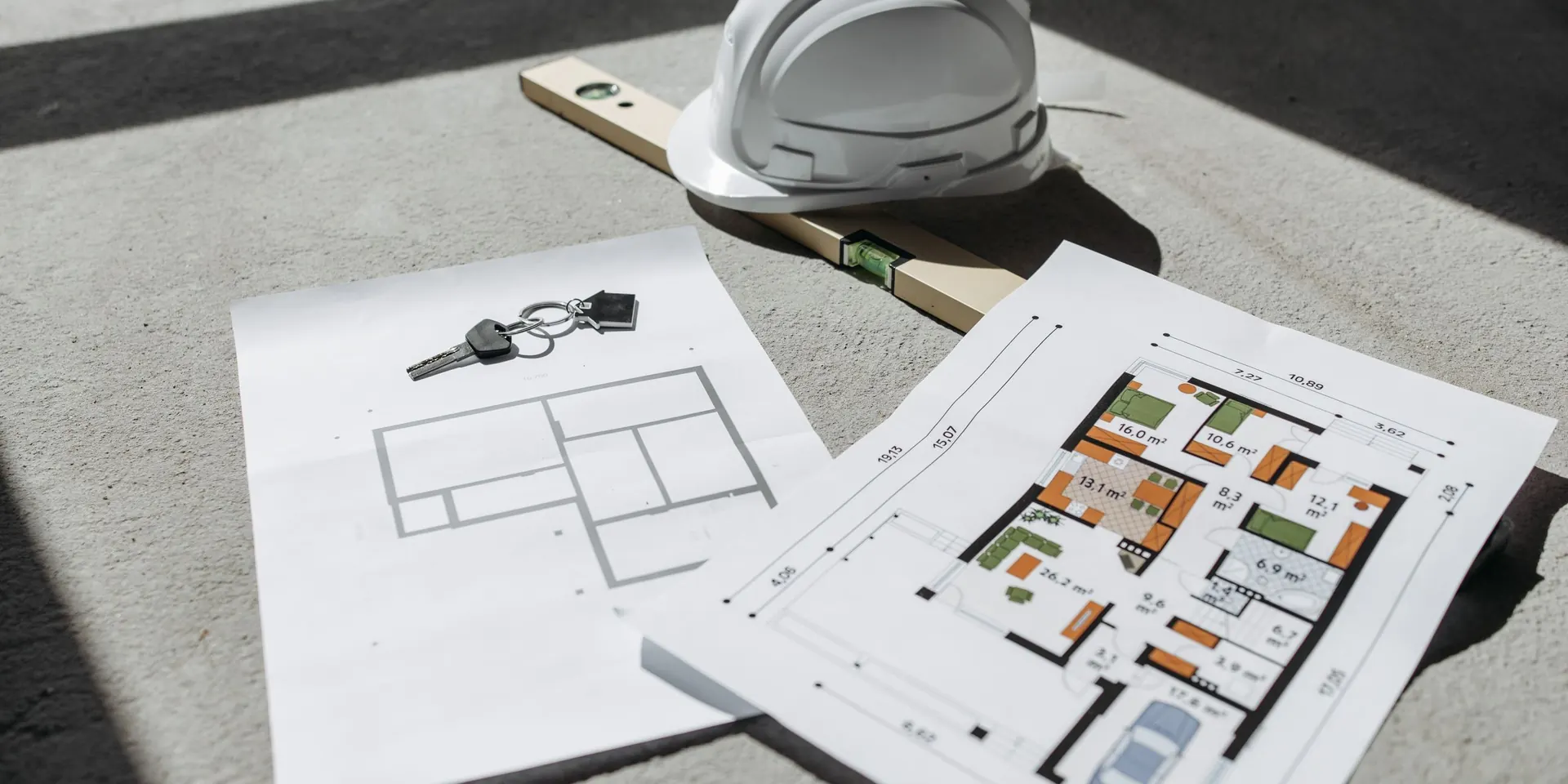 Casque de chantier, niveau, plans et clés posés au soleil sur une dalle, devis d'assurance décennale
