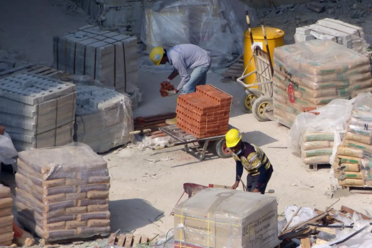 Ouvriers casqués manipulant briques et palettes de matériaux sur un chantier de construction