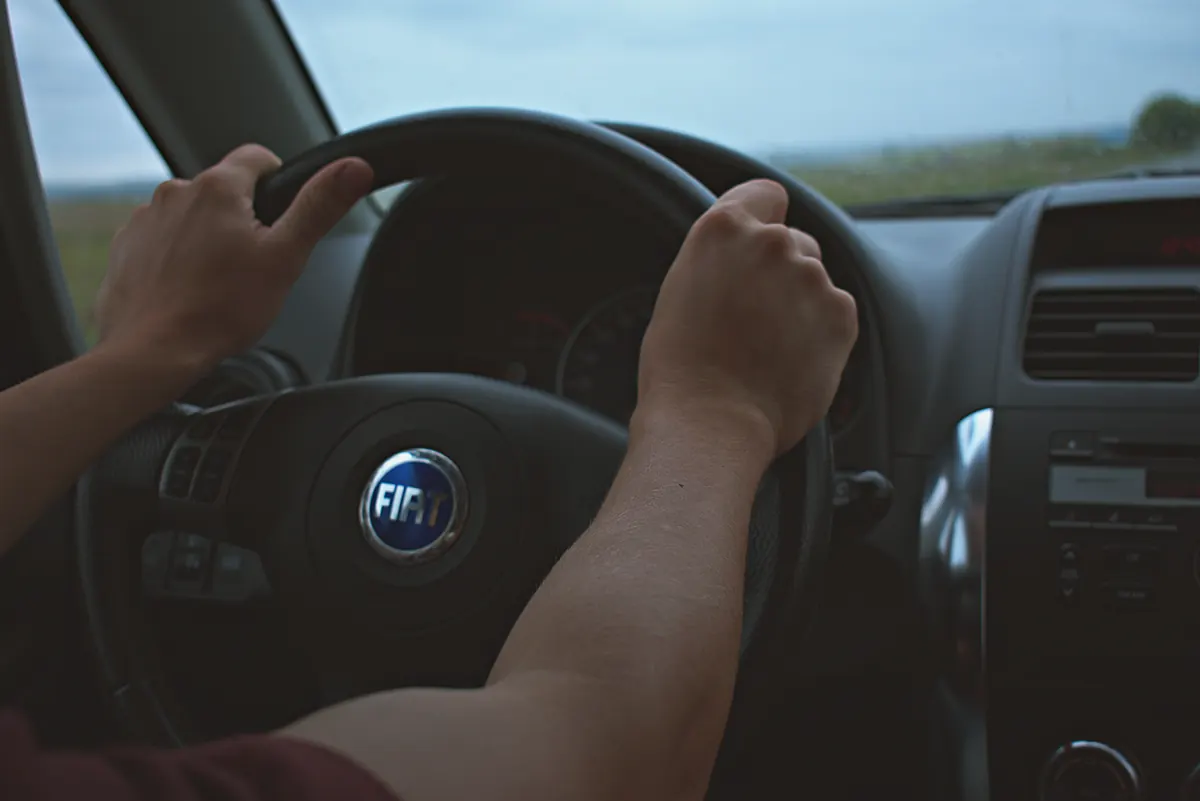 Mains d'un conducteur posées sur le volant d'une citadine en roulant à la campagne