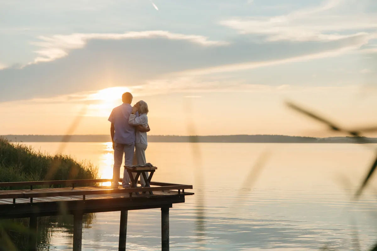 Couple de seniors enlacés sur un ponton au coucher du soleil, complémentaire santé senior