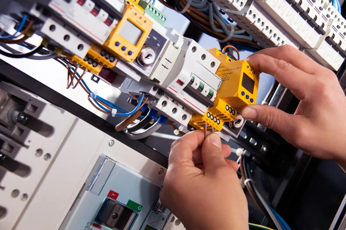 Mains d'un électricien câblant un tableau électrique équipé de disjoncteurs