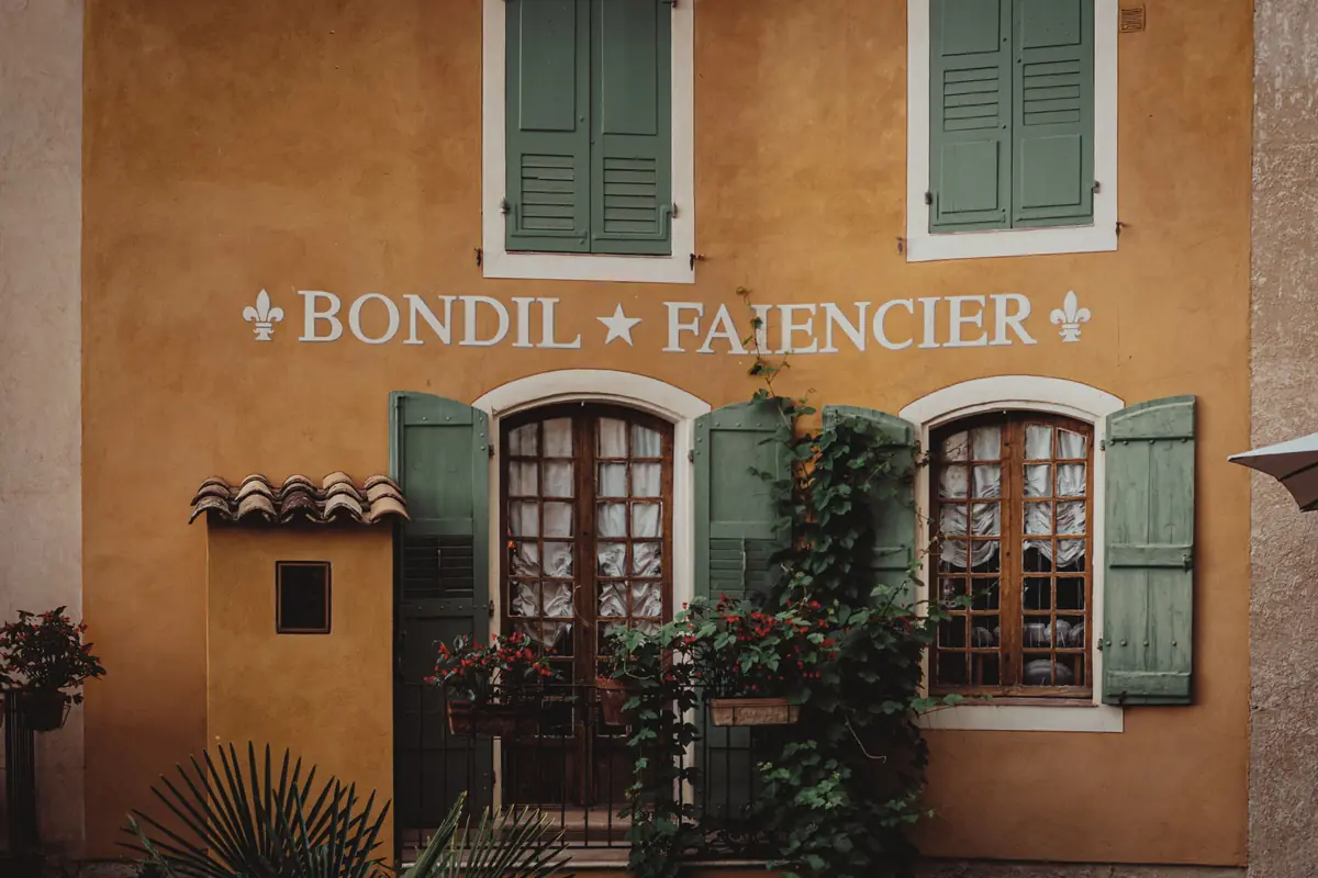 Façade ocre d'une maison ancienne aux volets verts et fenêtres cintrées
