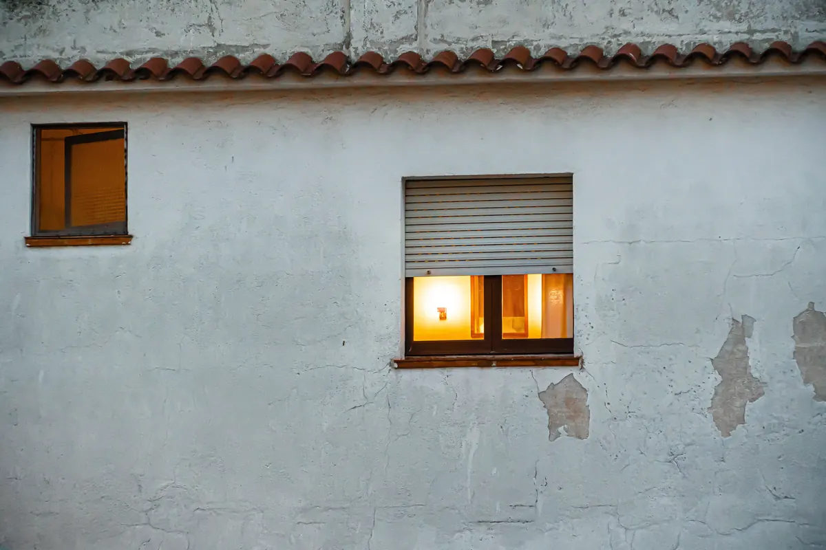 Fenêtre éclairée sur la façade crépie d'une maison au toit de tuiles, logement assuré