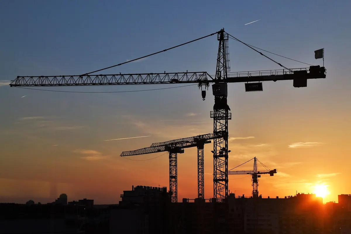 Grues de chantier se découpant sur un ciel orangé au coucher du soleil