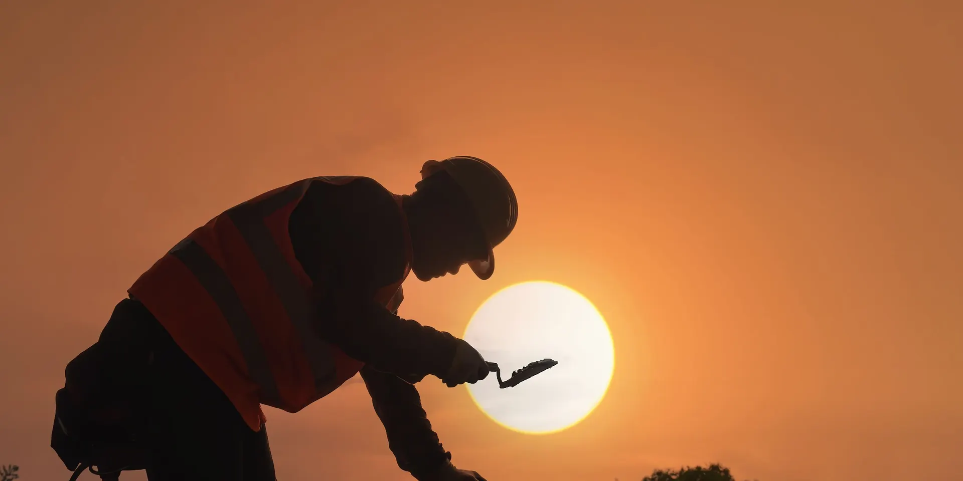 Silhouette d'un maçon maniant la truelle au coucher du soleil, pour l'assurance décennale des artisans du bâtiment