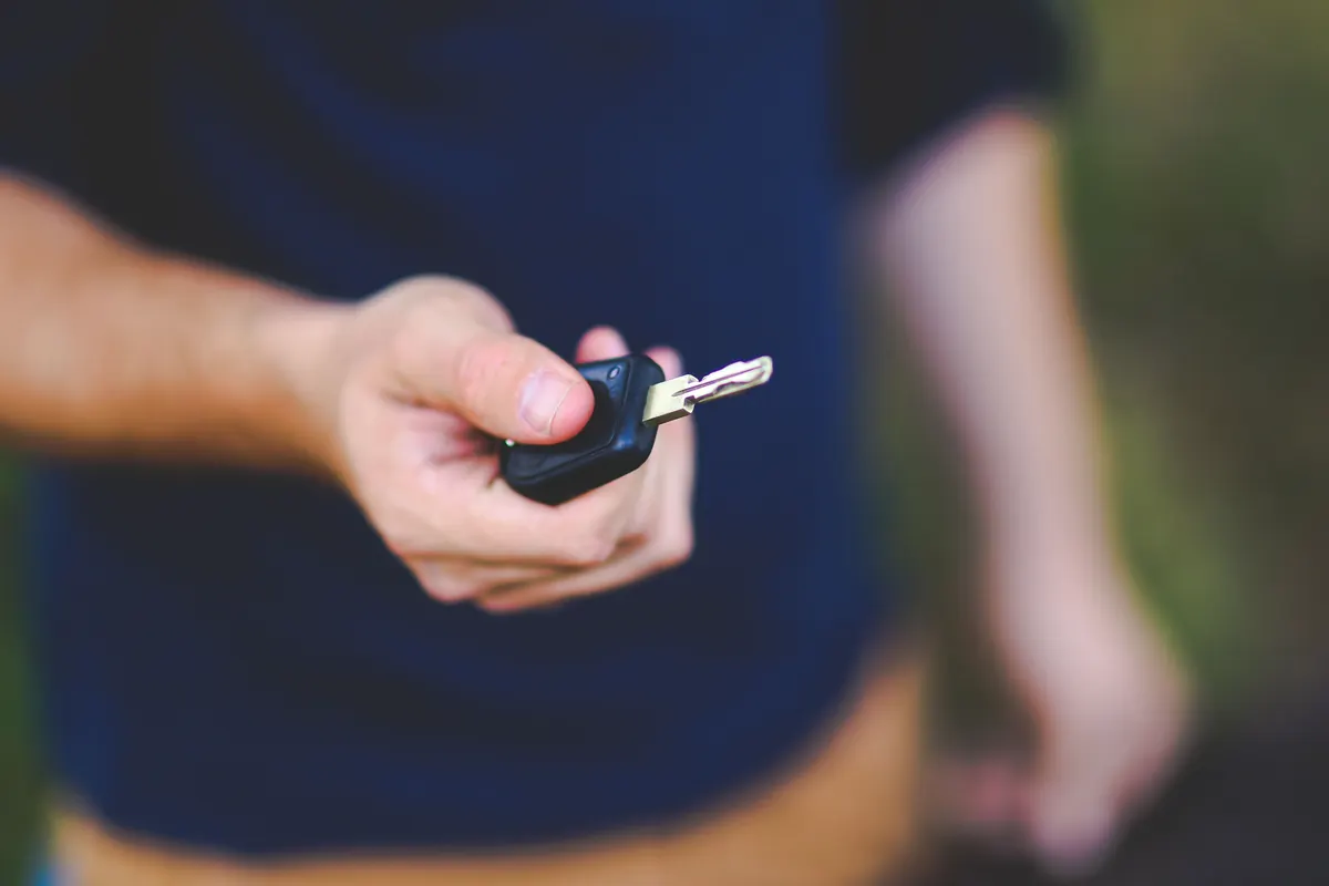 Main tendant une clé de voiture en extérieur, souscription d'une assurance auto