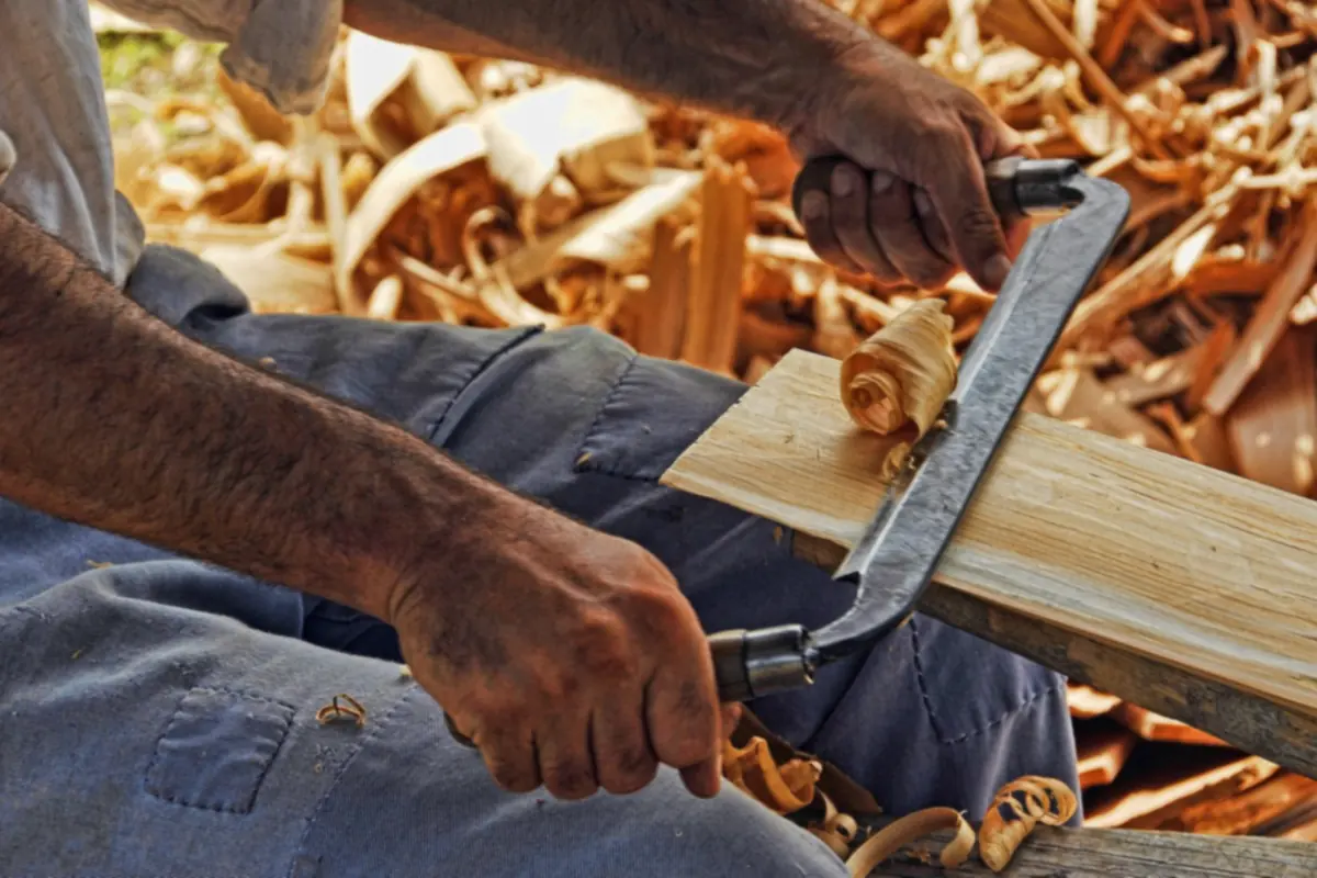 Mains d'un menuisier rabotant une planche au milieu des copeaux de bois