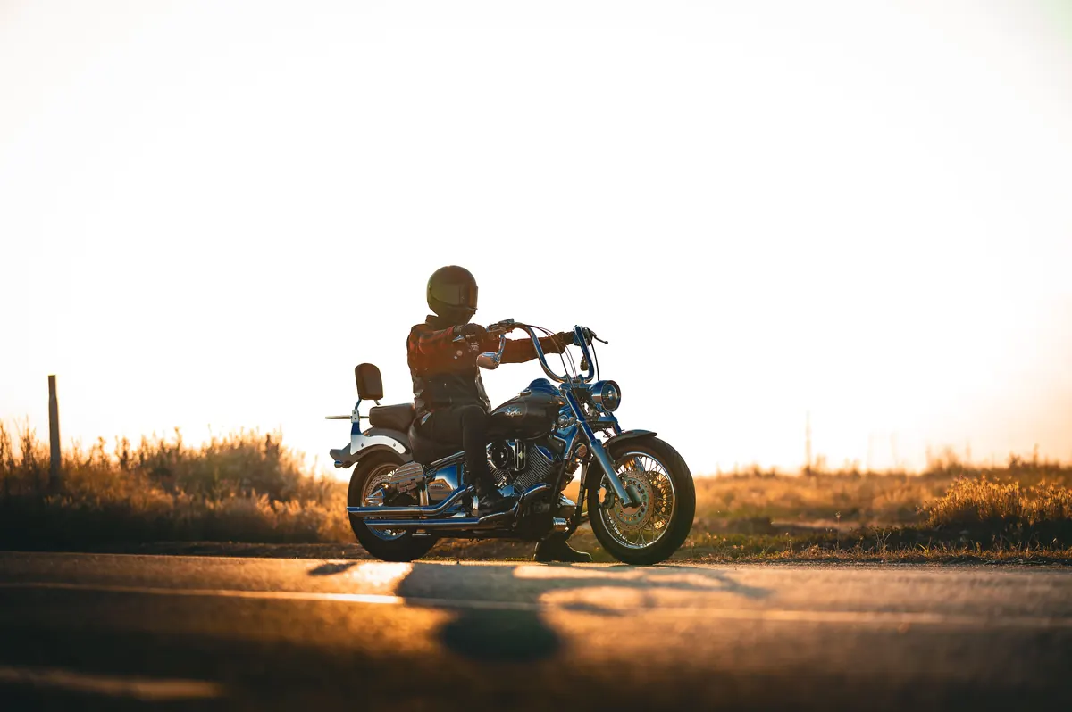Motard sur une route de campagne à contre-jour, herbes dorées en fin de journée
