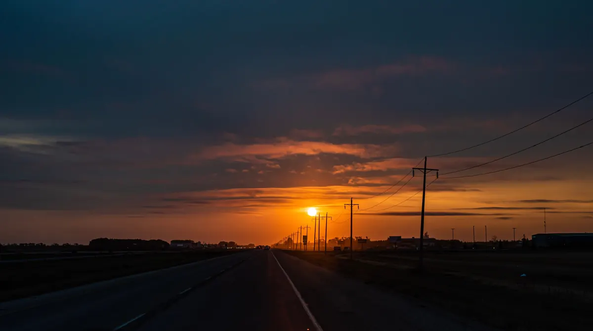 Route éclairée par des lampadaires au crépuscule, soleil couchant à l'horizon