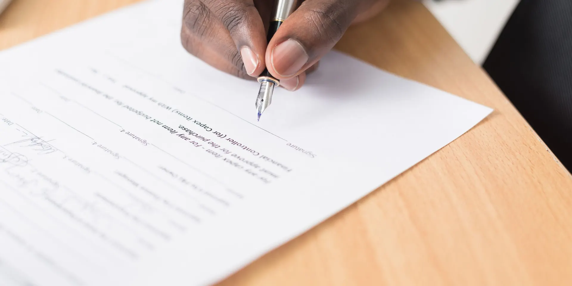 Main signant un document au stylo sur un bureau en bois, demande de devis d'assurance