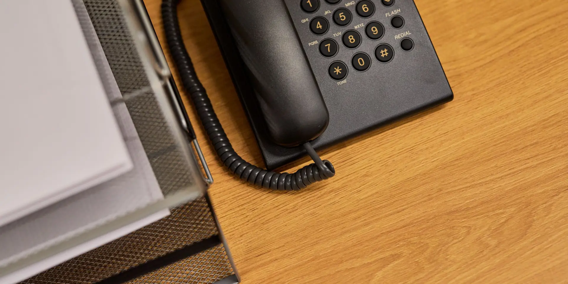 Téléphone de bureau noir et documents rangés sur un bureau en bois, pour contacter l'agence