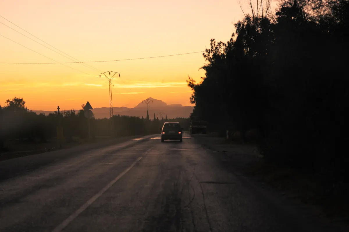 Voiture sur une route bordée d'arbres sous un ciel orangé, devis d'assurance auto